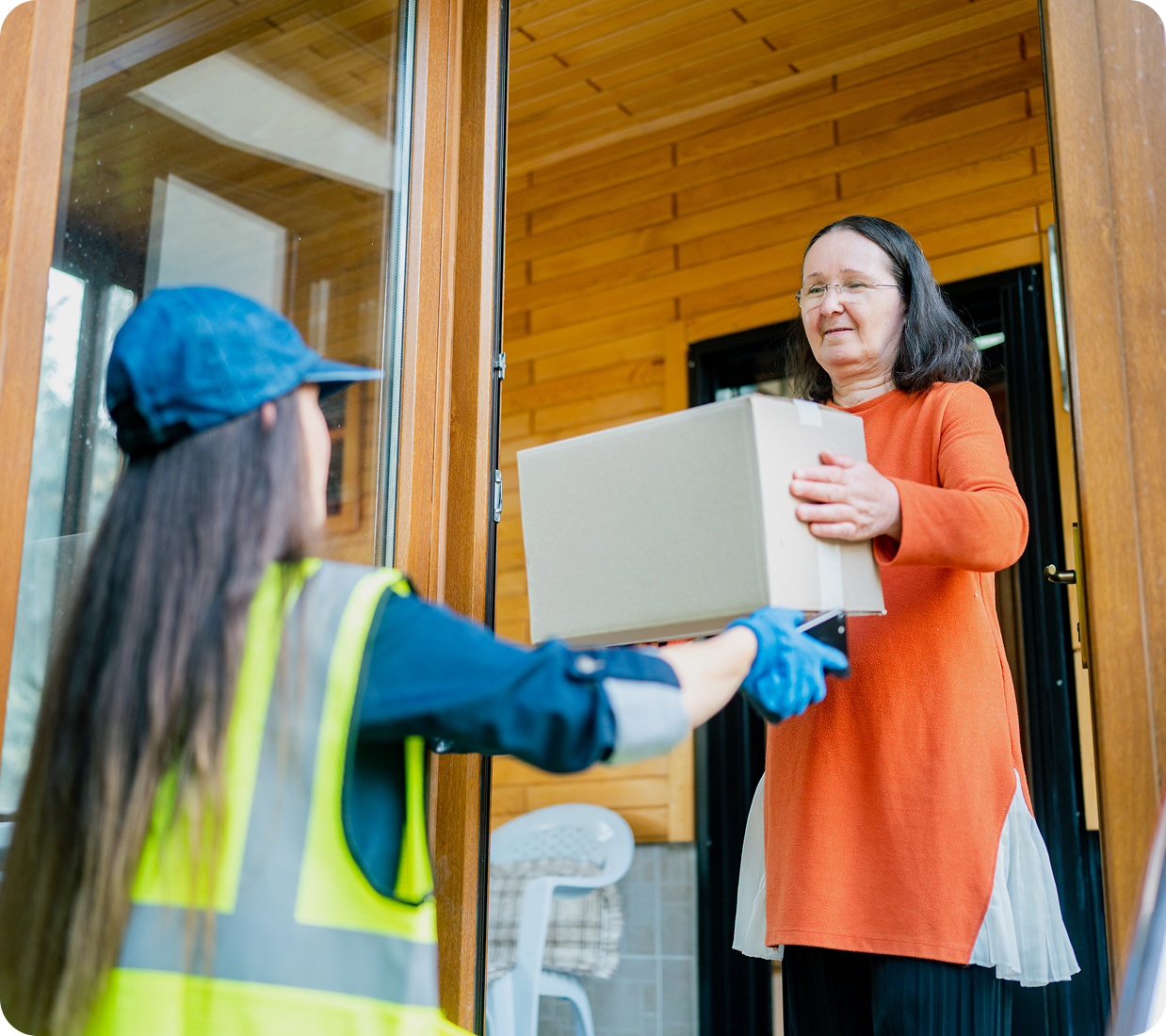 Delivery person handing package to woman indoors.